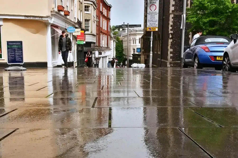 Rain-soaked British street with wet paving reflecting the sky, the kind of weather that wears out driveway sealer in north Manchester